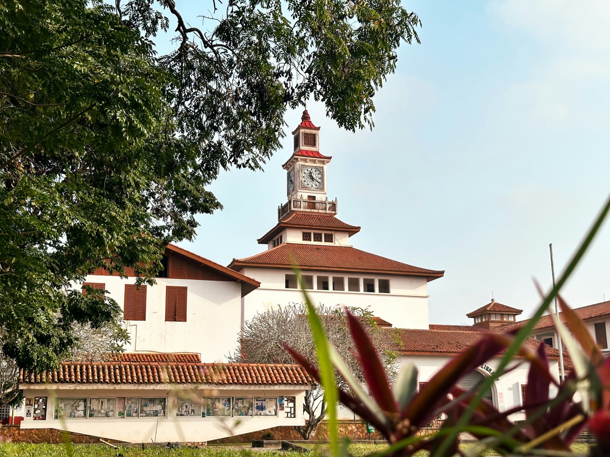 A university clock tower with a tiled roof, seen through trees on a campus